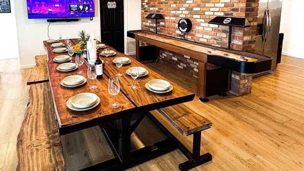 Une cuisine moderne avec un mur de fond en briques, un barbecue intégré et une longue table à manger pouvant accueillir six personnes.