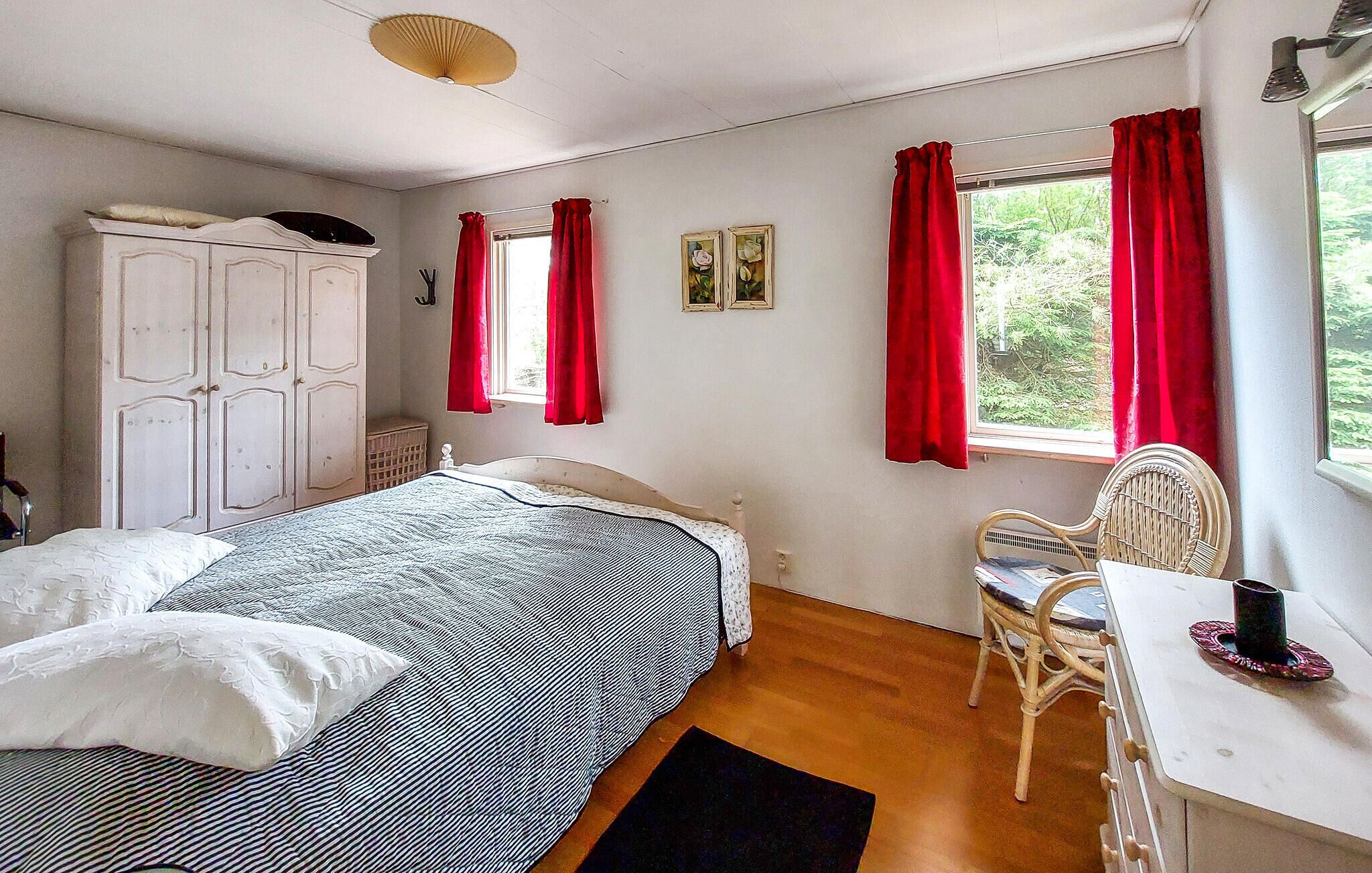 Une chambre à coucher avec un lit, un bureau, une chaise, une armoire et une fenêtre avec des rideaux rouges.
