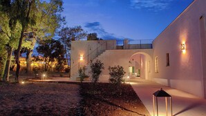 A modern building with a staircase leading to an upper level, surrounded by trees and illuminated by ambient lighting. - 4 bedroom condo in apulia (Puglia)