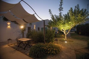 Un patio al aire libre con mesa y sillas, rodeado de plantas y un árbol.