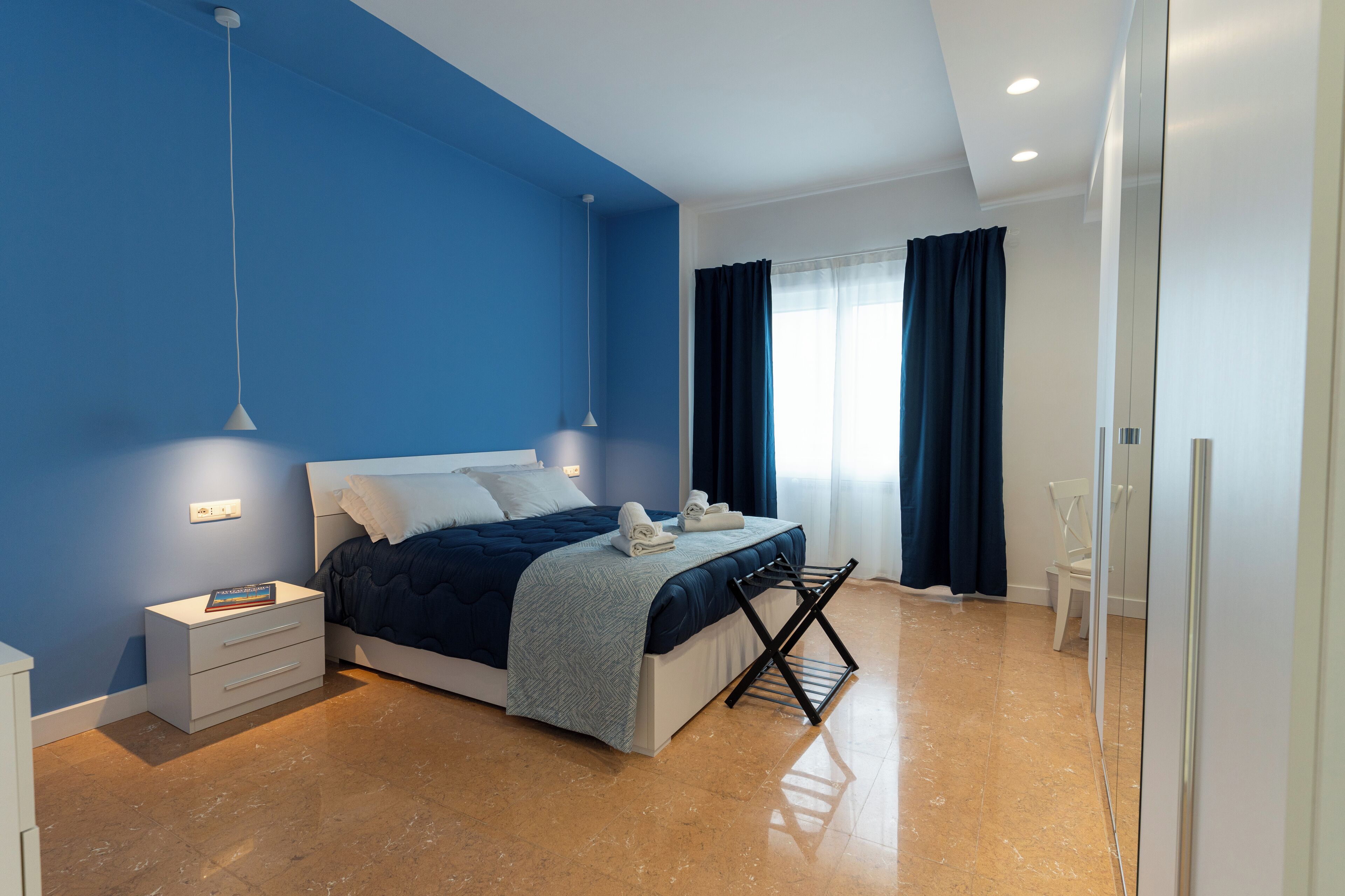 A modern bedroom with a bed, bedside tables, a hanging light fixture, and a window with curtains.