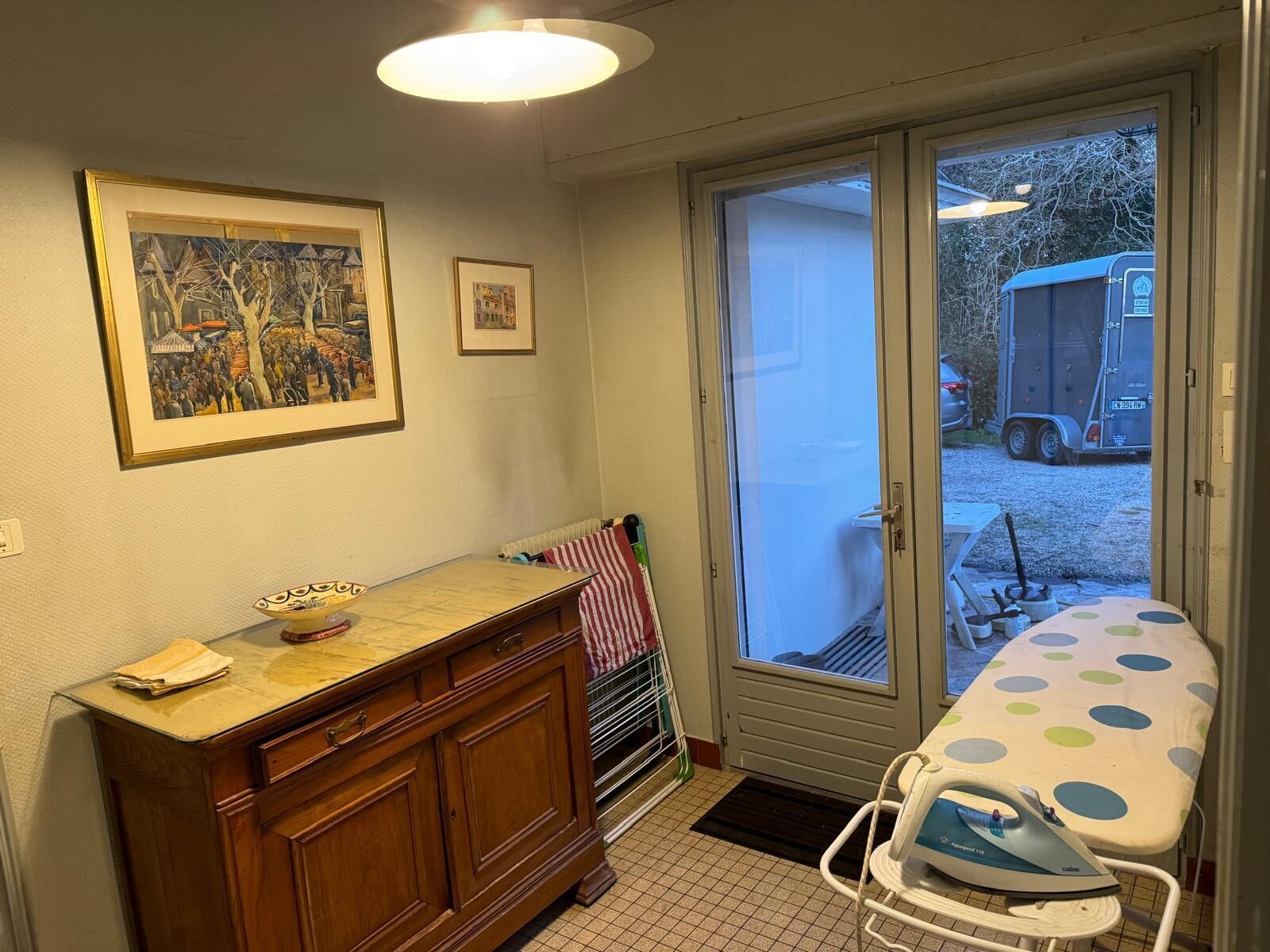 Una habitación con un armario de madera, una mesa de comedor con mantel de lunares y un ventanal corredero que da a un área exterior con una caravana estacionada.