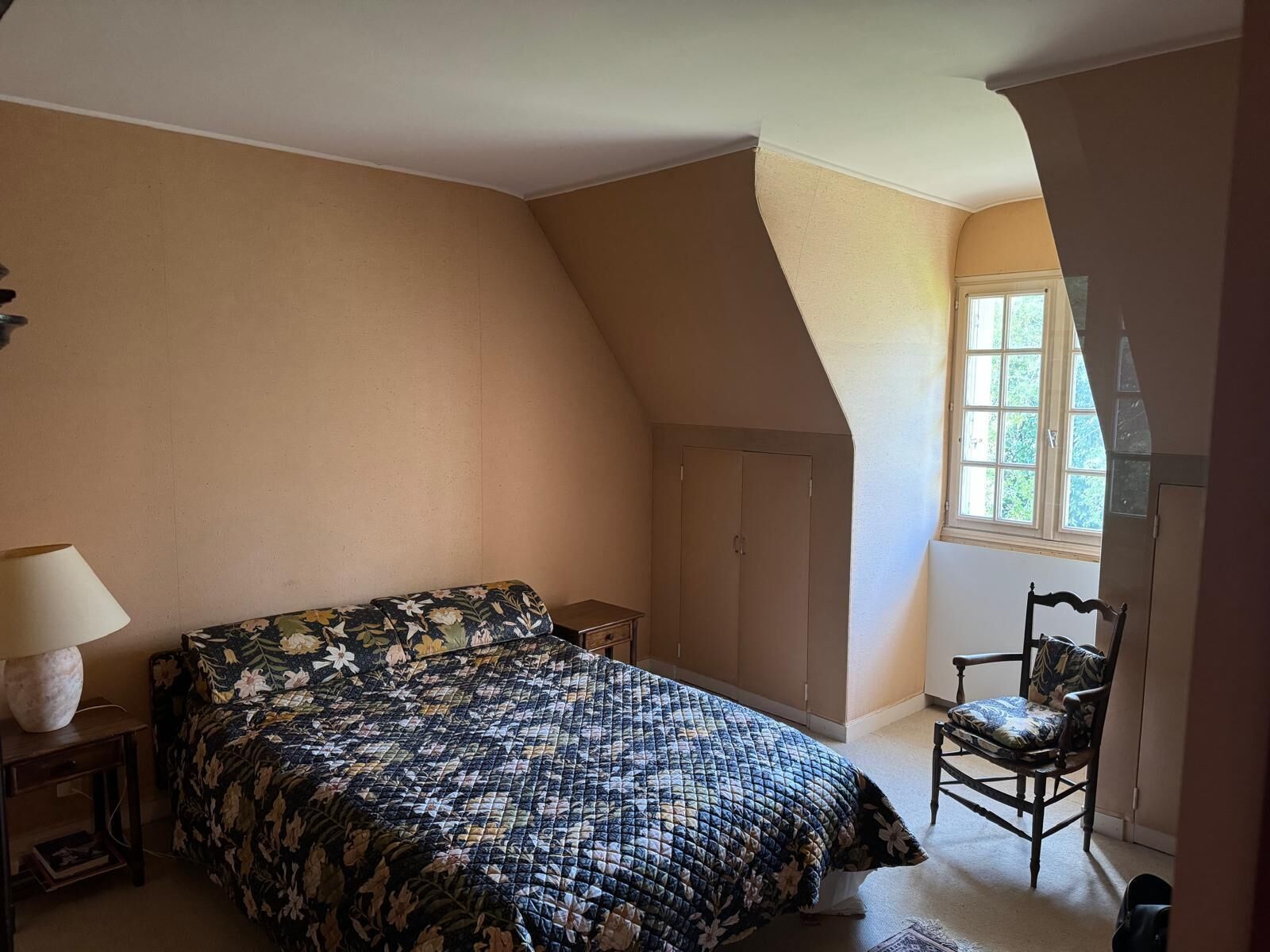 Un dormitorio con cama, una silla, una lámpara y ventana.