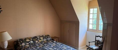 Un dormitorio con cama, una silla, una lámpara y ventana.