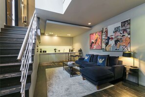 Una sala de estar moderna con un sofá azul oscuro, una mesa de centro y una escalera con barandilla metálica.