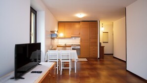 A modern kitchen with wooden cabinets, a dining table with chairs, a TV, and a remote control on a table. - La Casa di Andrea (Gardone Riviera)