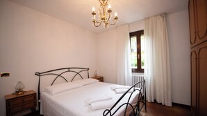 A bedroom with a bed, a nightstand, a lamp, a window with curtains, and a radiator. - La Casa di Andrea (Gardone Riviera)