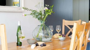 A wooden dining table with a clear glass vase containing flowers, a bottle of wine, glasses, and a bowl of grapes. - Clearwater House - sleeps 6 guests  in 3 bedrooms (Hayle)