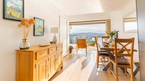 A modern dining area with a wooden table, chairs, and a view of the city through large windows. - Clearwater House - sleeps 6 guests  in 3 bedrooms (Hayle)