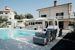 A swimming pool with lounge chairs and umbrellas, surrounded by a building with a balcony.