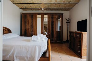 A bedroom with a bed, wooden wardrobe, and a television on a cabinet.