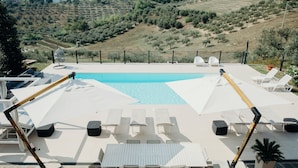 Zona de piscina al terrat amb gandules i ombrelles, envoltada d'un pati de pedra i amb vista a un paisatge ondulat.