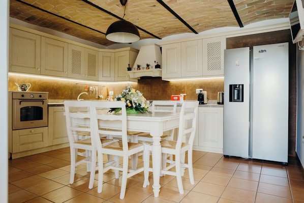 Una cocina con armarios blancos, una mesa de comedor con sillas, un refrigerador y una estufa.