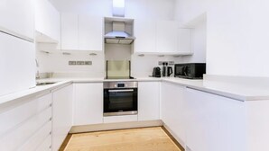 Una cocina moderna con armarios blancos, horno integrado, microondas y cafetera.