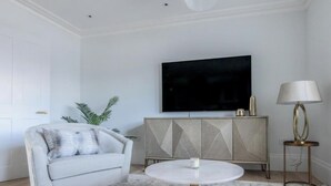 Una sala de estar moderna con un sofá blanco, una mesa redonda, un mueble con diseños geométricos, un televisor de pantalla plana y una lámpara de pie.