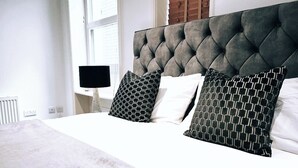 Una cama bien hecha con un cabecero capitonado, dos almohadas estampadas y una colcha blanca.