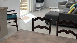Ein Wohnzimmer mit grauem Sofa, Fernseher, Esstisch mit Stühlen und einer Treppe, die zu einem Außenbereich führt.