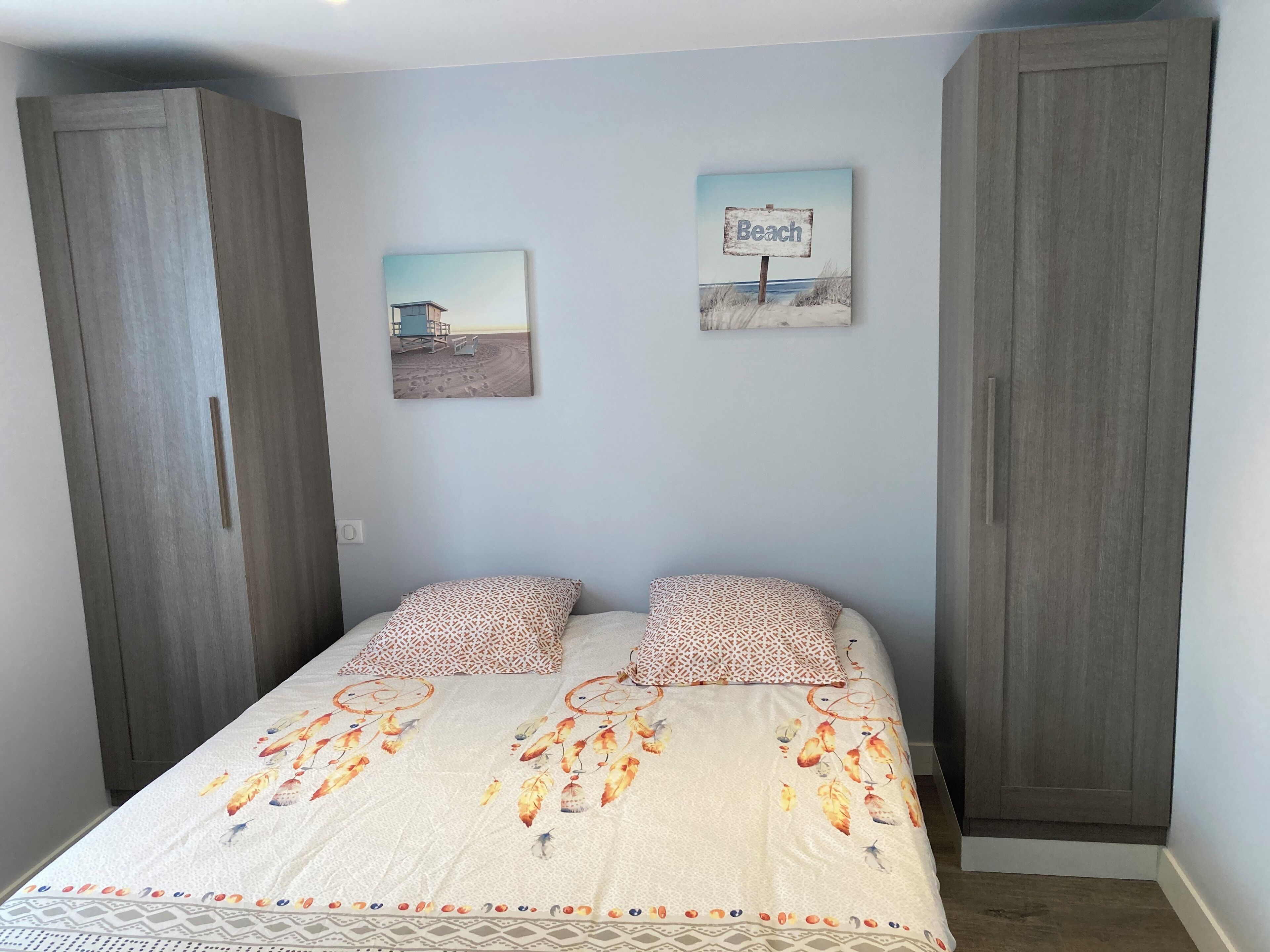 Une chambre à coucher avec un lit, deux oreillers, un mur orné de deux tableaux et une armoire.