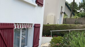 Ein weißes Gebäude mit roten Fensterläden, einem Kiesweg und einem Garten mit verschiedenen Pflanzen und Blumen.