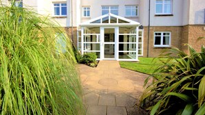A building with a white glass conservatory in the center, surrounded by a paved walkway and greenery.