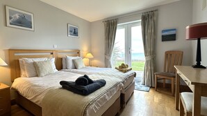 A hotel room with a bed, a desk, a chair, and a view of the sea.
