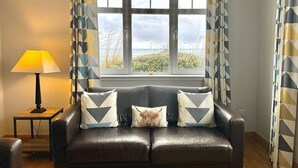 A living room with a leather sofa, patterned cushions, a lamp, and a window with curtains.