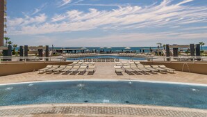 A pool area with sun loungers and a view of the ocean.