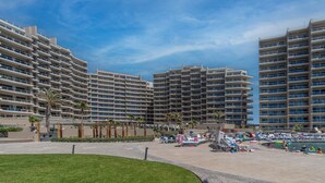 A modern hotel with multiple high-rise buildings, a pool area with lounge chairs and umbrellas, and palm trees.