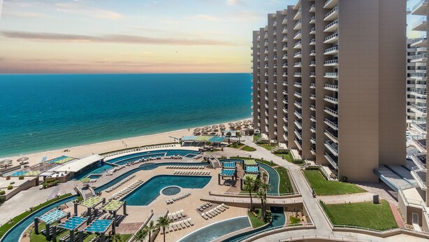 Ein Resort mit mehreren Schwimmbecken, einer Strandanlage und einem Hochhaus mit Balkonen.