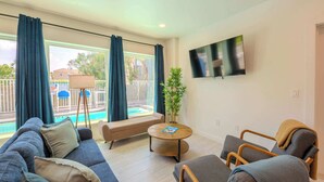 Een moderne woonkamer met een bank, fauteuils, een salontafel en een aan de muur bevestigde televisie.