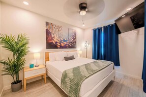 A modern hotel room with a bed, a nightstand, a potted plant, and a ceiling fan.