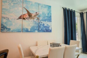 A dining area with a marble table, cushioned chairs, and a large painting of a sea turtle.