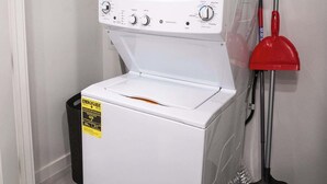 Una unidad de lavadora y secadora de carga frontal blanca con panel de control, un trapeador rojo y un cubo de basura.