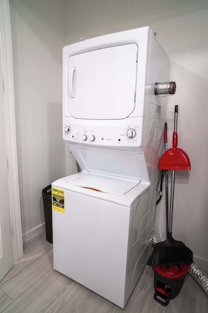 Una unidad de lavadora y secadora de carga frontal blanca con panel de control, un trapeador rojo y un cubo de basura.