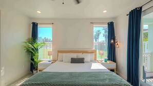 Een hotelkamer met een bed, nachtkastje, lamp, potplant en uitzicht op de omgeving.