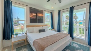 Habitación de hotel con una cama grande, ventilador de techo, mesita de noche, ventana con cortinas y vistas al exterior.