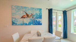Een eetruimte met een witte tafel, vier witte stoelen en een blauw kunstwerk aan de muur.