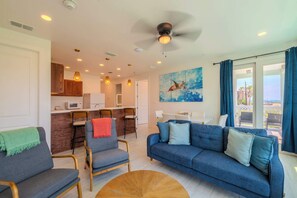 A modern living room with a blue sofa, two armchairs, a wooden coffee table, and a kitchen area visible in the background. - Banana Bay Retreat (South Padre Island)