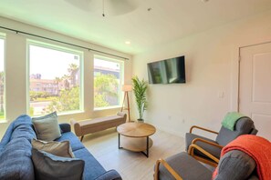 Un salon moderne avec un canapé, des fauteuils, une table basse ronde et un téléviseur fixé au mur.