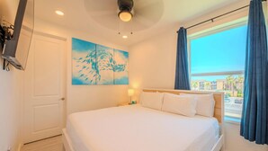 A hotel room with a bed, a painting, a window with curtains, and a ceiling light. - Pineapple Paradise (South Padre Island)