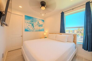 A hotel room with a bed, a painting, a window with curtains, and a ceiling light. - Pineapple Paradise (South Padre Island)