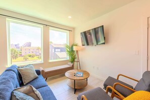 A modern living room with a sofa, armchairs, a round coffee table, and a TV mounted on the wall.