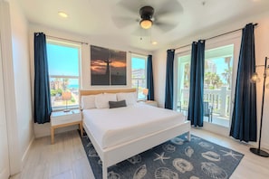 Habitación de hotel con cama, mesita de noche, lámpara, ventilador de techo y vistas al exterior.