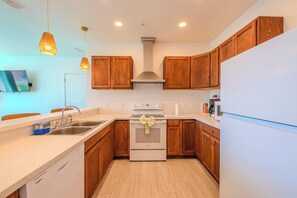 A modern kitchen with wooden cabinets, a stainless steel sink, a white dishwasher, and a stove with a decorative bow.