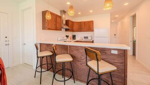 A modern kitchen with wooden cabinets, a central island with bar stools, and pendant lighting. - Pineapple Paradise (South Padre Island)