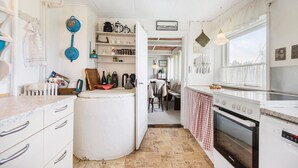 Una cocina con armarios blancos, una estufa y una ventana. Se observan estantes con utensilios de cocina y una puerta que da a otra habitación.