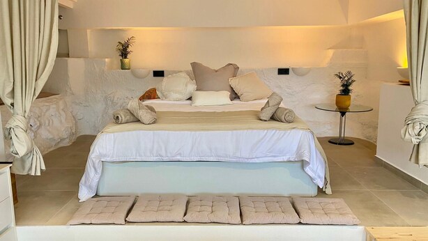A spacious bedroom with a large bed, multiple pillows, a bedside table, and a small round table with a plant. - Loft Rodeado de Tranquilidad (Sant Pere de Ribes)