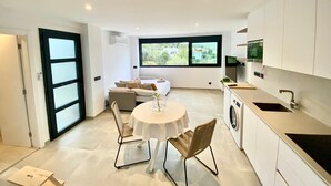 A modern kitchen with a dining area, a washing machine, and a large window offering a view of greenery. - Loft Rodeado de Tranquilidad (Sant Pere de Ribes)