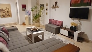 A modern living room with a grey sectional sofa, a coffee table, a TV mounted on the wall, and a large painting. - VILLA WITH PRIVATE POOL  (Hurghada)