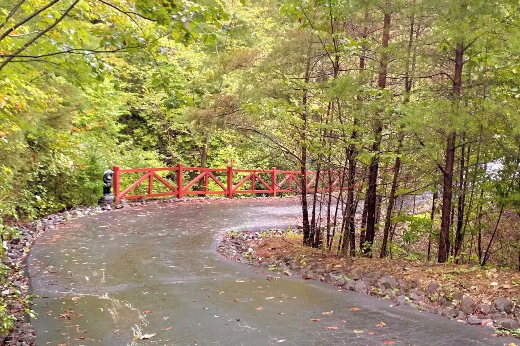 A winding road with a red bridge and a statue on the left.
